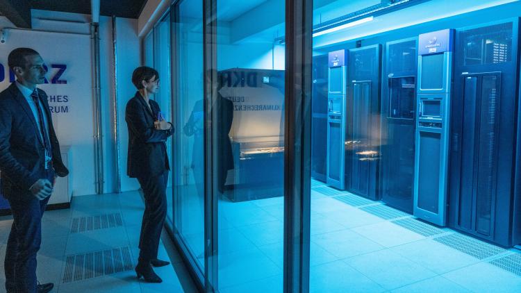 Das Foto zeigt Forschungsministerin Bettina Stark-Watzinger. Sie steht in einem blau ausgeleuchteten Raum und besichtigt technisches Gerät durch eine Glasfront.
