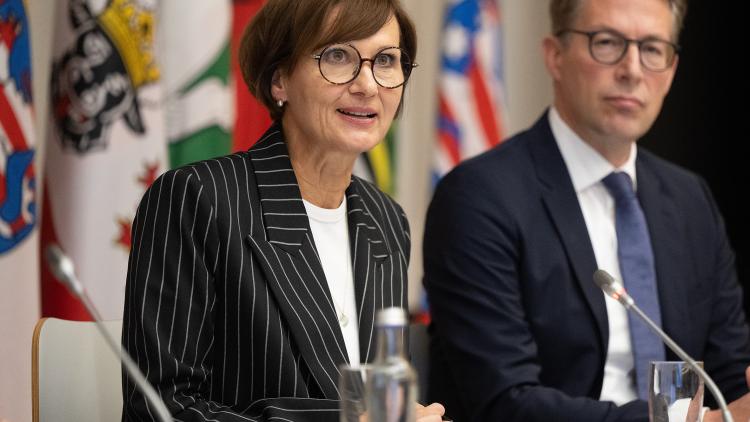 Bettina Stark-Watzinger und Markus Blume sitzen an einem Tisch mit Mikrofonen und geben eine Pressekonferenz, hinter ihnen sind die Flaggen der Bundesländer zu sehen